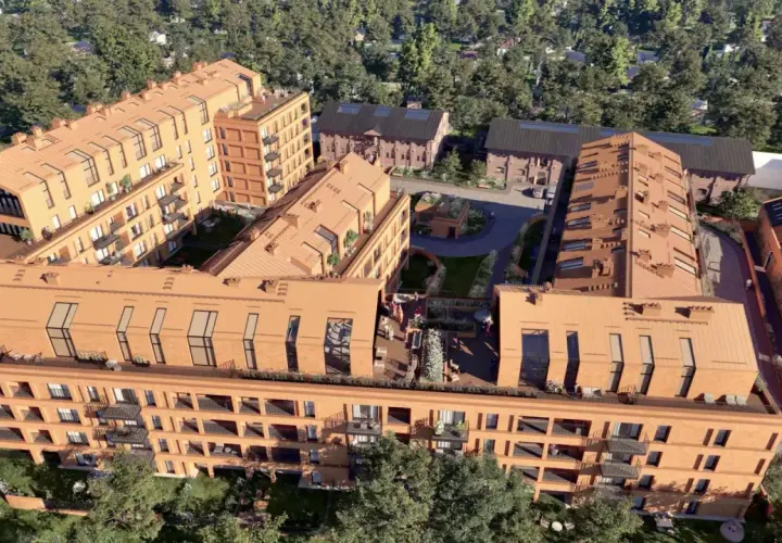Nowoczesne budynki mieszkalne nawiązujące architekturą do historycznego folwarku Scheiblera. Widać ceglane elewacje, spadziste dachy i zielone dziedzińce.
