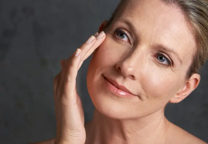 Une femme touche délicatement son visage, révélant une peau mature. La question "peau mature à partir de quel âge" se pose naturellement.