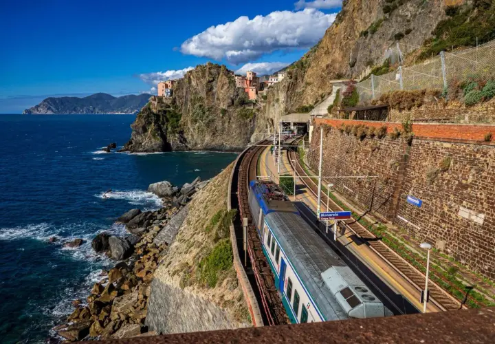 Zug fährt entlang der Küste von Cinque Terre. Bunte Häuser kleben an steilen Felsen über dem blauen Meer.