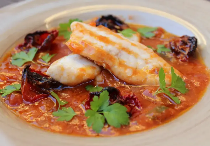 Deliciosa ventresca de merluza en salsa de tomate con pimientos secos y perejil fresco.