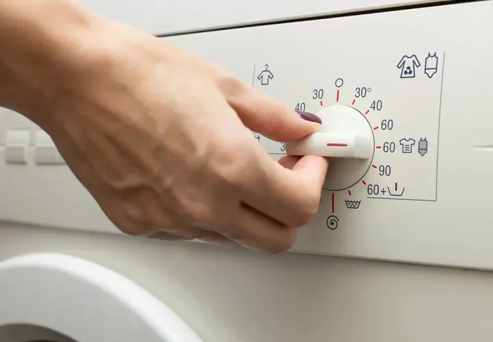 Main d'une personne réglant le bouton d'une machine à laver pour le lavage de vêtements.