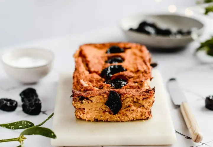 Domowy pasztet z resztek mięsa pieczonego, ozdobiony śliwkami, na desce z nożem i miseczką sosu.