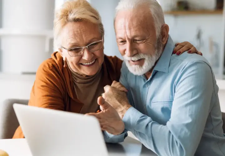 Uśmiechnięta para seniorów korzystająca z laptopa.