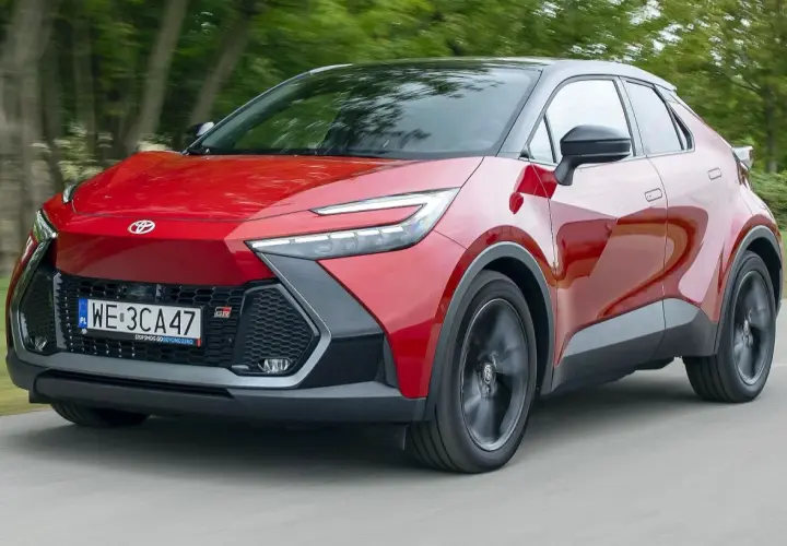Czerwona Toyota C-HR 2020 z czarnym dachem pędzi po drodze, otoczona zielenią drzew.