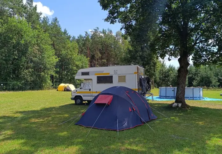 Namiot i kamper na trawie, w tle las i basen. Idealne miejsce na **camping Świętokrzyskie**.