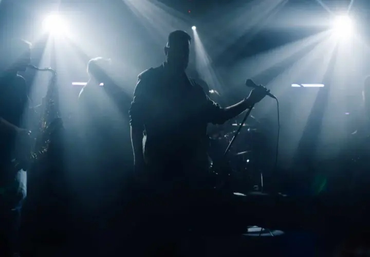 Zespół na scenie, wokalista z mikrofonem, saksofonista. Czy bilety imienne na koncert sprawdzają?
