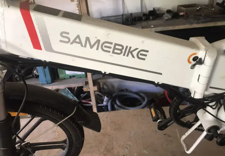 Biały rower elektryczny SAMEBIKE, z czerwonym i szarym paskiem, stoi w warsztacie. Wspomaganie nie działa, co jest frustrujące.