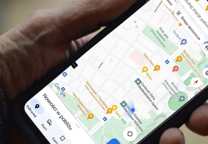 Dłoń trzyma telefon z mapą Google. Widoczna jest opcja udostępnianie lokalizacji, a także pobliskie restauracje i sklepy.