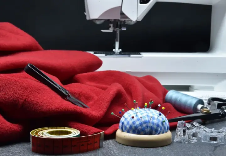 Czerwony materiał, maszyna do szycia, szpilki, miarka i nożyczki – wszystko gotowe do tworzenia patchwork projektów.