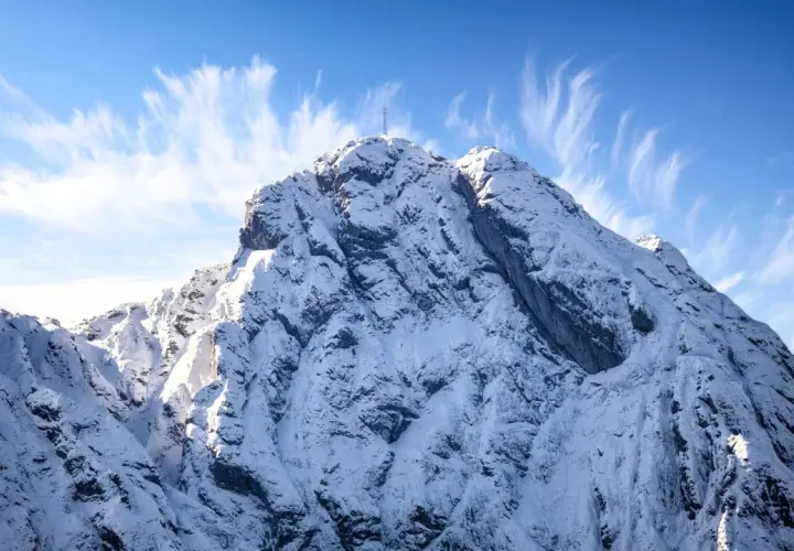 Ośnieżony szczyt Giewontu z krzyżem, pod błękitnym niebem z pierzastymi chmurami. Zastanawiasz się, ile trwa wejście na Giewont?