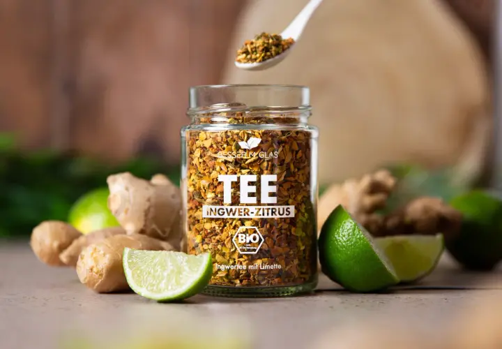 Glas mit Ingwer-Zitrus-Tee, frischem Ingwer und Limetten. Perfekt für einen wärmenden Tee, der lange ziehen kann.