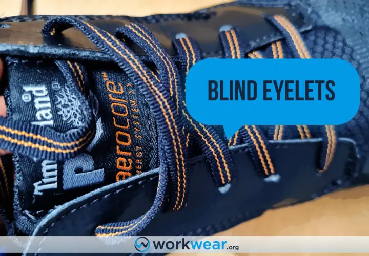 Close-up of a dark blue Timberland boot with orange stitching. The laces go through what are called blind eyelets, a feature that keeps them secure.