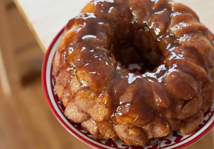 Delizioso monkey bread dorato, ricoperto di glassa lucida, servito su un piatto con bordo rosso.