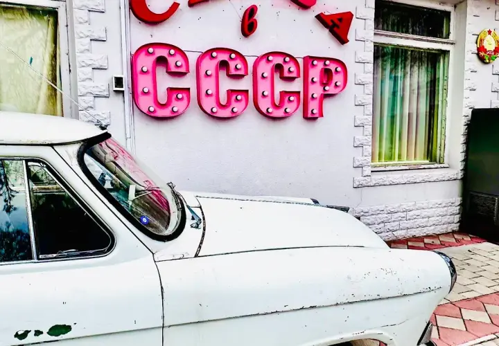 Biały, stary samochód przed budynkiem z neonem CCCP. Czy to podróż w czasie do tamtych lat?