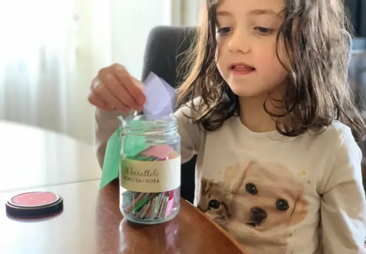 Bambina inserisce un bigliettino nel barattolo "Scaccia-Noia", pieno di idee per giochi da fare quando ci si annoia.