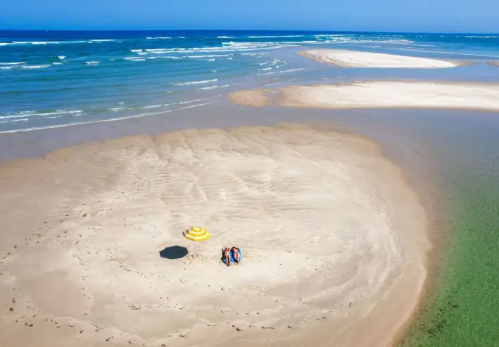 Dos personas descansan bajo una sombrilla a rayas en una playa de arena en Ria Formosa. El mar azul y las aguas cristalinas rodean la isla.