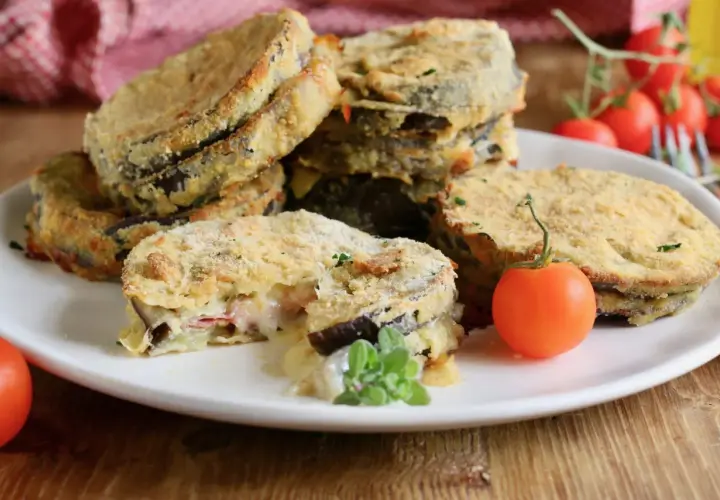 Deliziosi cordon bleu di melanzane impanati e fritti, con un ripieno filante di formaggio e prosciutto, guarniti con pomodorini freschi.