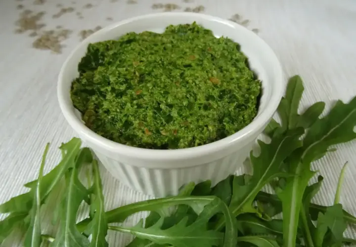 Pesto z rukoli w białej miseczce, otoczone świeżymi liśćmi rukoli. Idealne do makaronu lub jako dodatek do kanapek.