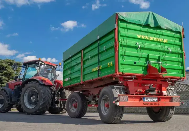 Czerwony traktor z zieloną przyczepą. Zastanawiasz się, ile można jechać z przyczepką? Ten zestaw jest gotowy do pracy.