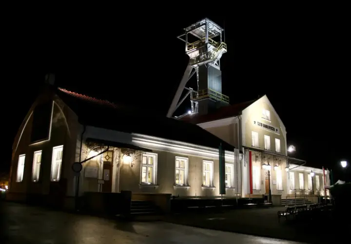 Wieczorem przy szybie kopalni Wieliczka, gdzie można kupić bilety, widać oświetlone budynki i wieżę wyciągową.