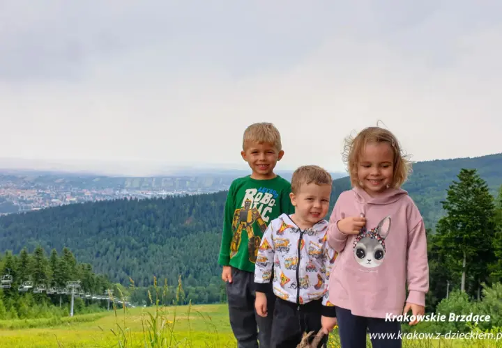 Trójka uśmiechniętych dzieci na tle górskiego krajobrazu z wyciągiem krzesełkowym. Idealne chełm atrakcje dla dzieci na wakacje.