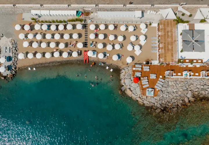 Vue aérienne d'une plage de Diano Marina avec des parasols blancs, des chaises longues, des baigneurs dans la mer turquoise et un jacuzzi sur la jetée.