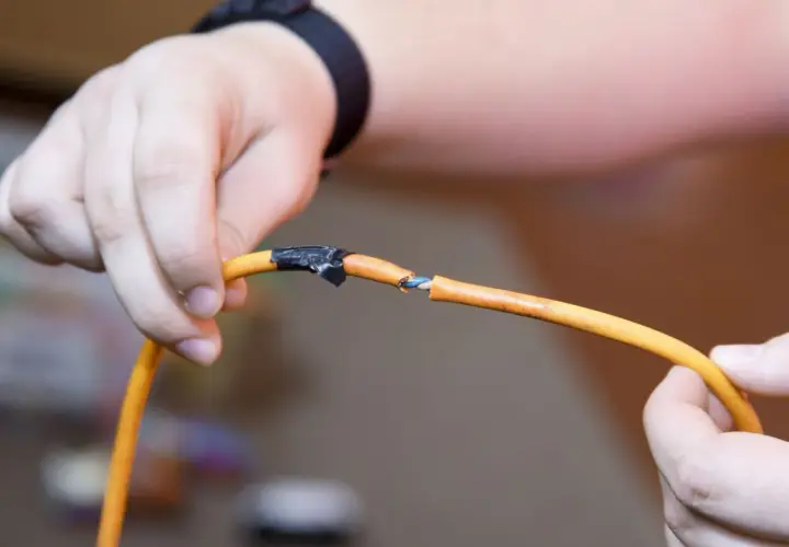 Dłonie trzymają przecięty pomarańczowy kabel elektryczny, pokazując, jak połączyć przecięty kabel elektryczny przy użyciu taśmy izolacyjnej.