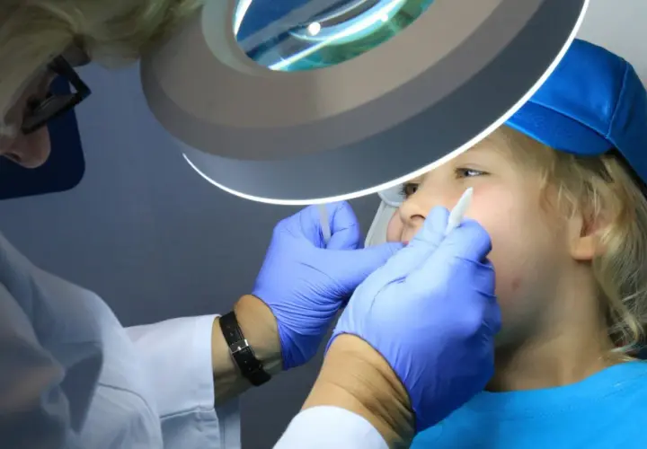 Dentysta w rękawiczkach bada usta dziecka pod lampą powiększającą.