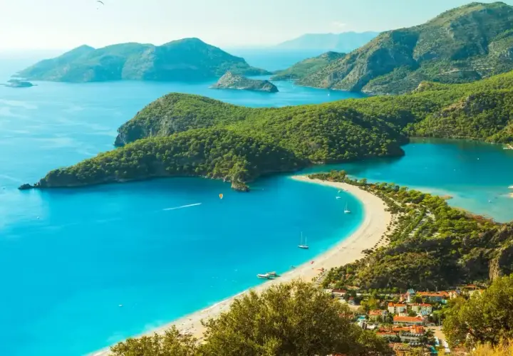 Turcja zachwyca turkusowym morzem i zielonymi wzgórzami. Widok na zatokę z plażą i łodziami.