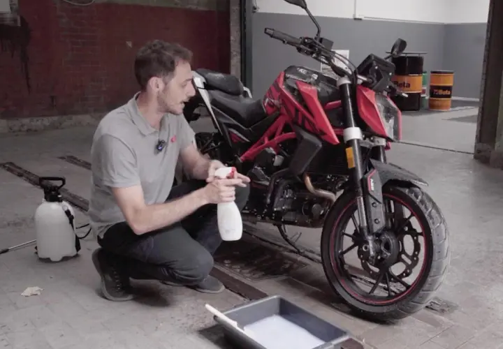 Uomo con spray e secchio di schiuma, pronto a usare prodotti casalinghi per lavare moto.