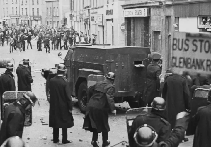 Unruhen in Nordirland, ein gepanzertes Fahrzeug und Polizisten mit Schilden. Die Szene erinnert an die Zeit vor dem Karfreitagsabkommen.