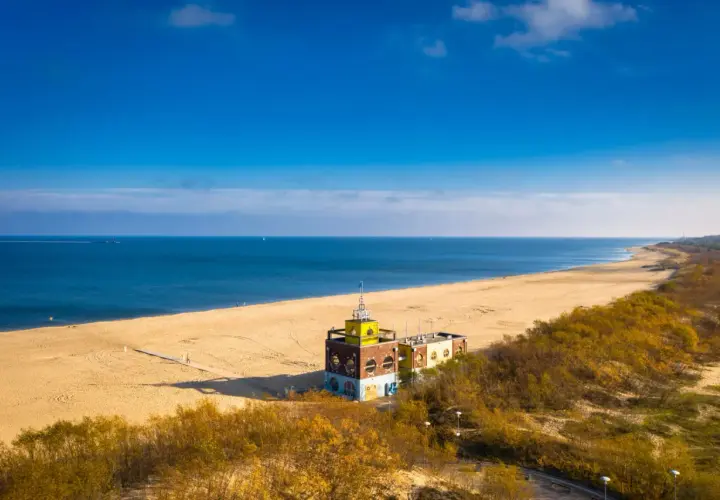 Piękna plaża i morze, idealne na spacer po jednej z **miejscowości nad morzem koło Gdańska**. W oddali widać charakterystyczny budynek.