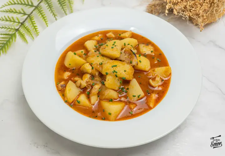 Plato de patatas con sepia, un guiso casero que evoca las patatas con sepia de la abuela, con trozos de patata y sepia en una salsa rojiza.