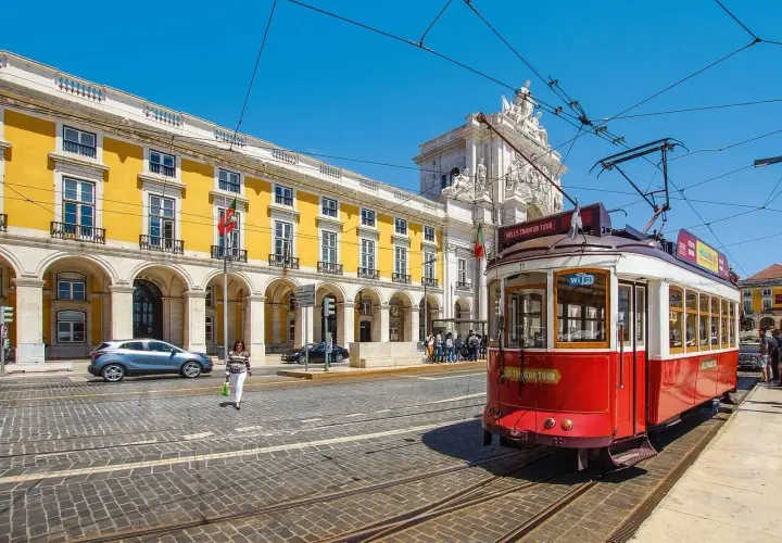 Tranvía rojo en Lisboa, listo para llevarte de Lisboa al Algarve. Edificio amarillo y arco triunfal al fondo.