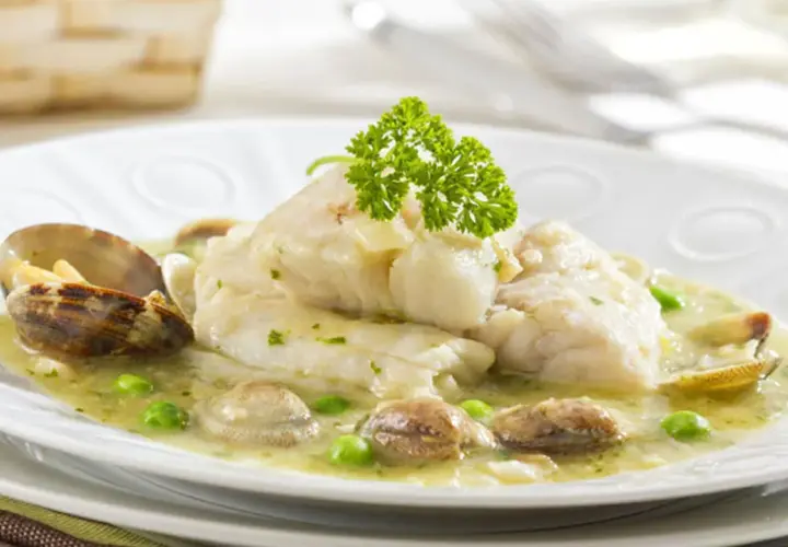 Merluza en salsa verde con almejas y guisantes, decorada con perejil fresco. Un plato marinero delicioso.