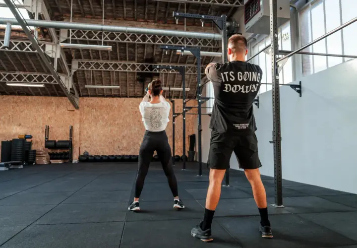 Para pozuje na siłowni. Ona wykonuje ćwiczenie z kettlebell, on stoi z tyłu. To właśnie crossfit co to za trening!