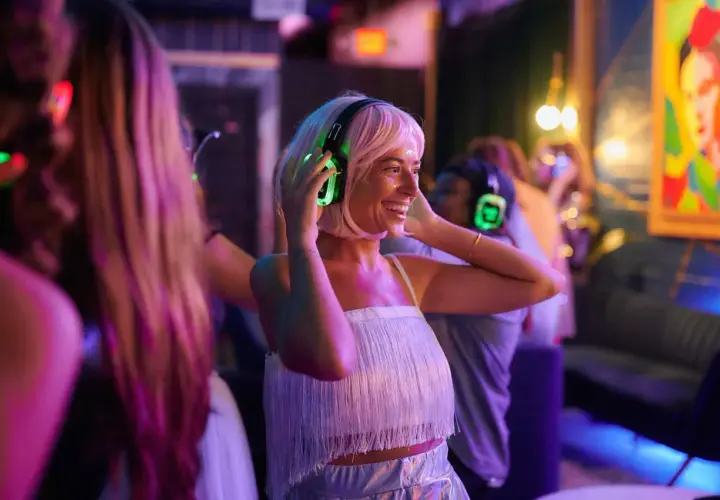 Uśmiechnięta kobieta z blond włosami cieszy się imprezą w stylu silent disco, zakładając świecące na zielono słuchawki.