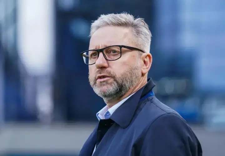 Brzęczek trener w okularach, z siwą brodą i włosami, w granatowej kurtce, patrzy w bok.