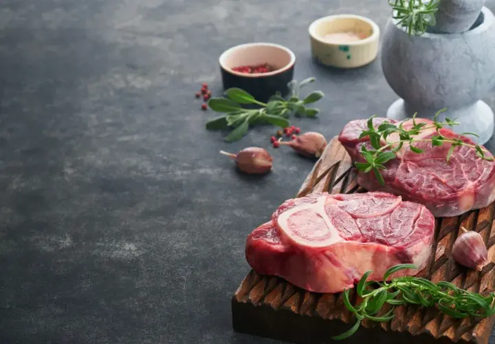Deux grosses pièces de viande au barbecue, prêtes à être grillées, avec des herbes fraîches et de l'ail.