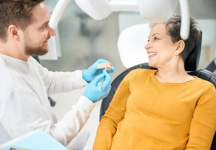 Dentista mostra un modello di denti a una paziente sorridente, discutendo di impianti dentali per un sorriso perfetto.