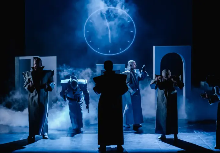 Postacie w futurystycznych strojach na scenie Teatru Arlekin w Łodzi. W tle świecący zegar.