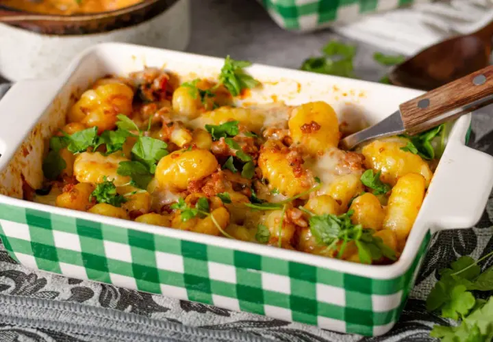 Zapiekane gnocchi z pomidorami i mozzarellą, posypane świeżą natką pietruszki, w zielono-białej kratce. Pyszne danie gotowe do podania.