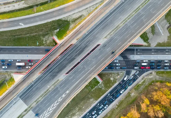 Widok z lotu ptaka na wielopasmową drogę, która może być najdłuższą ulicą w Warszawie. Samochody poruszają się po betonowych pasach.