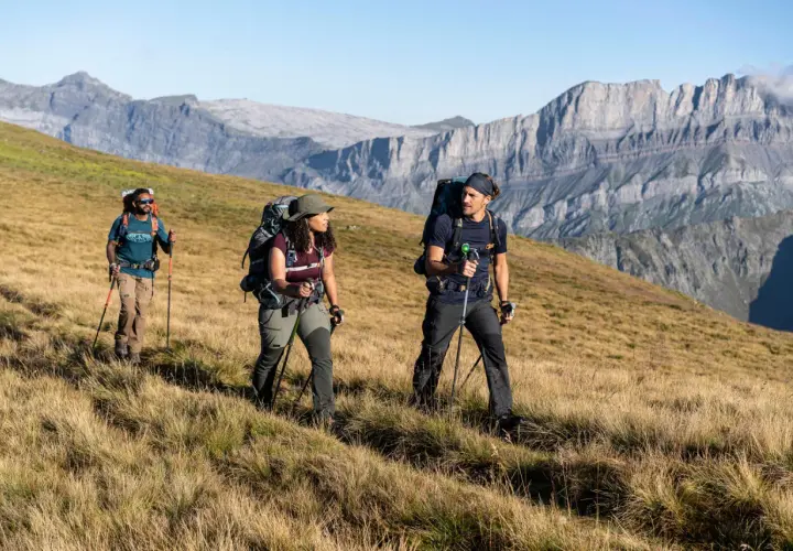 Trzech turystów z plecakami i kijkami przemierza górski szlak, przypominający **Pacific Crest Trail**.