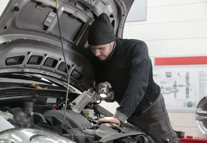 Mechanik samochodowy z latarką bada silnik. Zastanawiasz się, ile zarabia elektronik samochodowy?