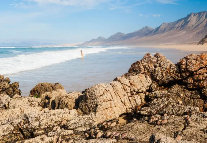 Una persona disfruta de las playas nudistas de Cantabria, con olas rompiendo en la costa y montañas al fondo.
