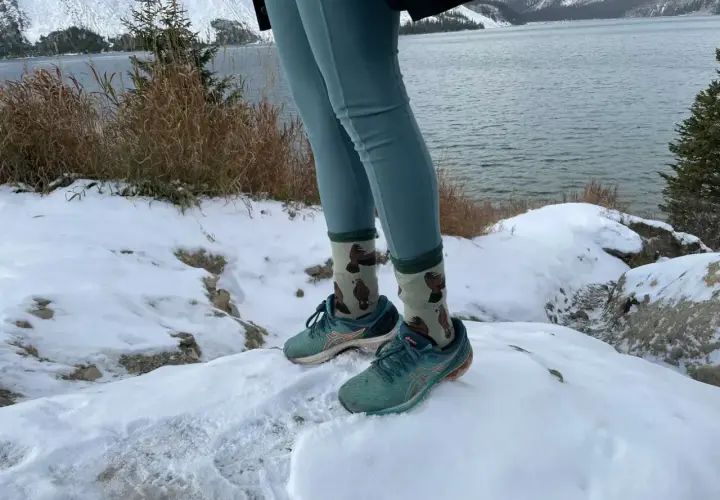 Wygodne leginsy w góry i buty do biegania na śniegu. W tle jezioro i ośnieżone szczyty.