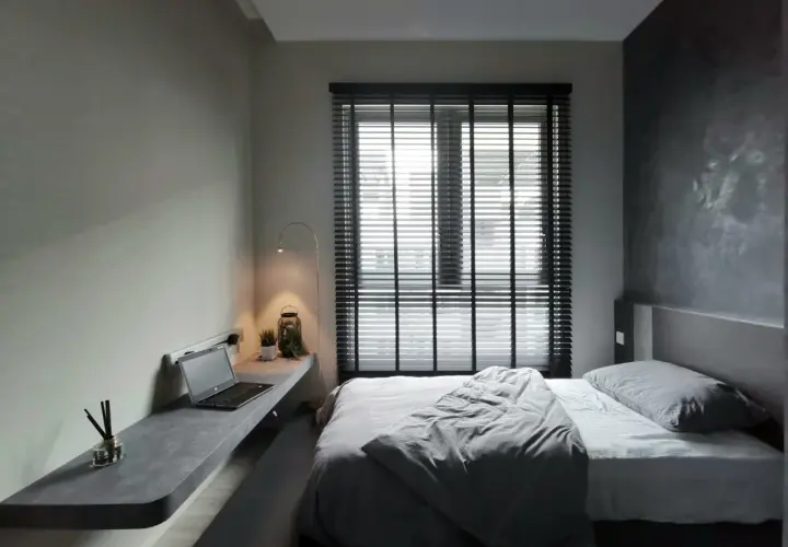 Nowoczesna, szara sypialnia z minimalistycznym biurkiem, laptopem i wygodnym łóżkiem.