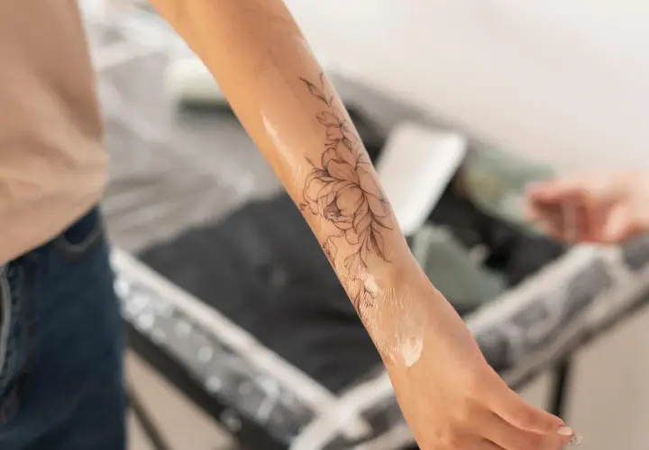 Un bras orné d'un tatouage floral délicat, la peau légèrement humide, comme si elle commençait à peler après la séance.