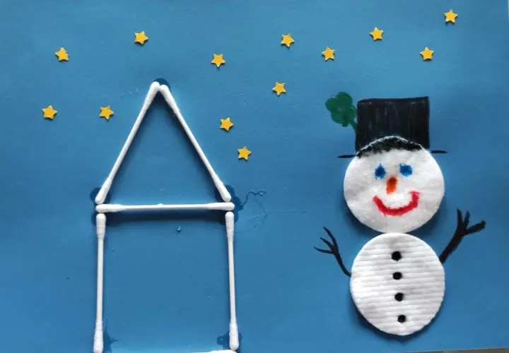Ein fröhlicher schneemann aus wattepads steht vor einem Haus aus Wattestäbchen. Kleine gelbe Sterne funkeln am blauen Himmel.